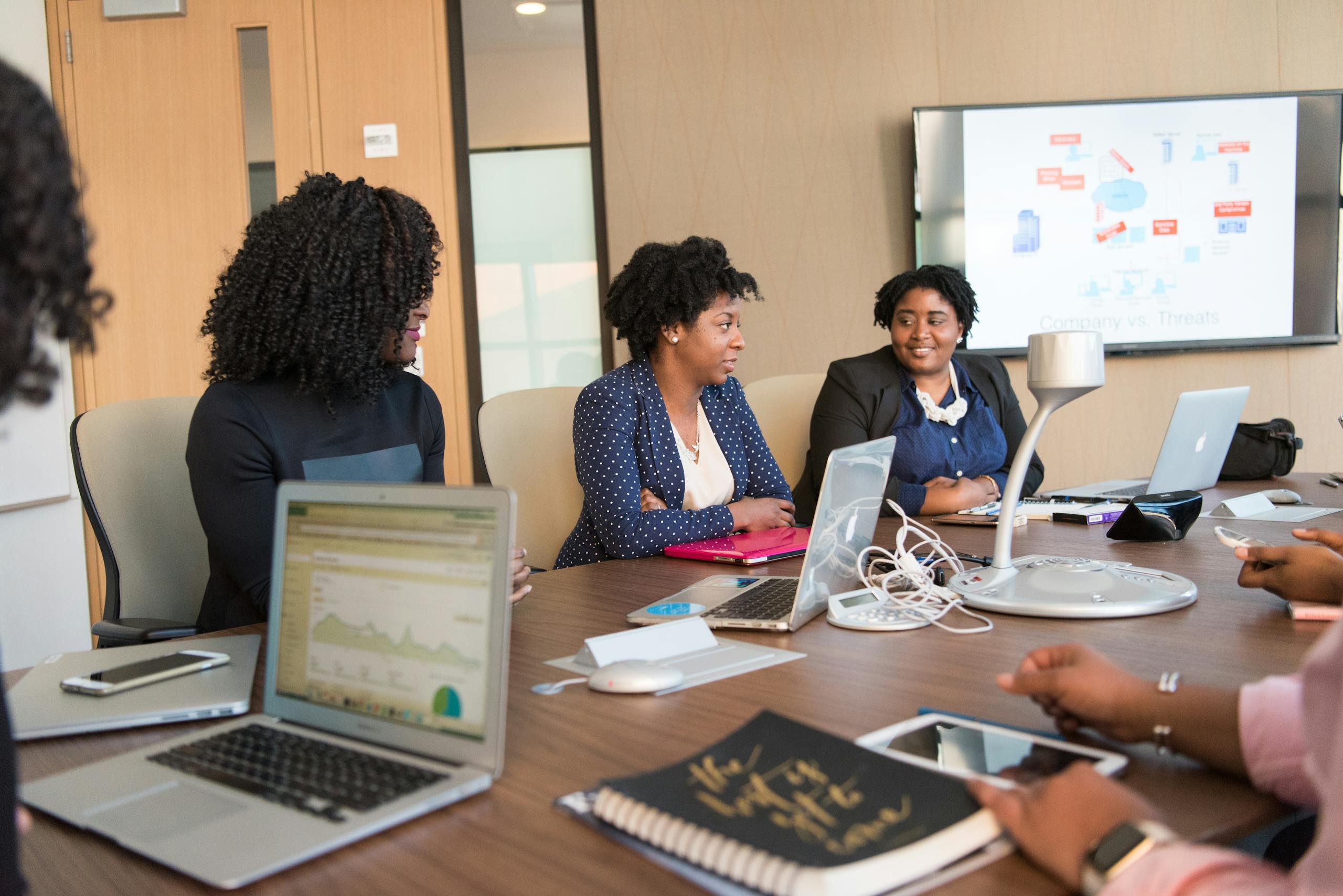 Four diverse women engaged in a business meeting with laptops and presentations in an office.