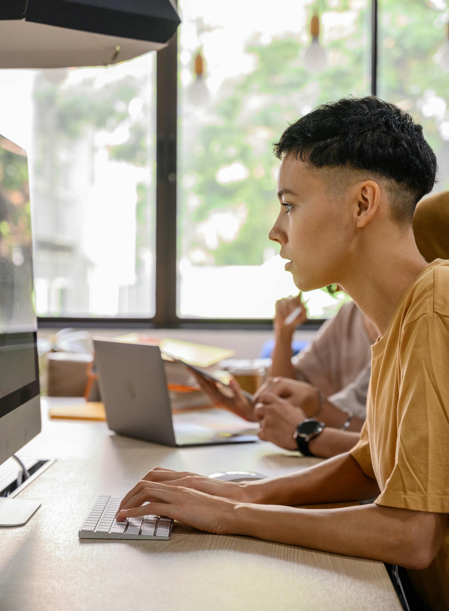 Teenager attentively working on desktop computer in a bright, modern office environment.